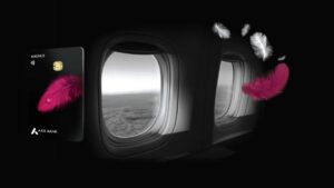 A black Axis Bank Magnus Credit Card with a pink feather design floating next to two dark airplane windows, suggesting high-end air travel.