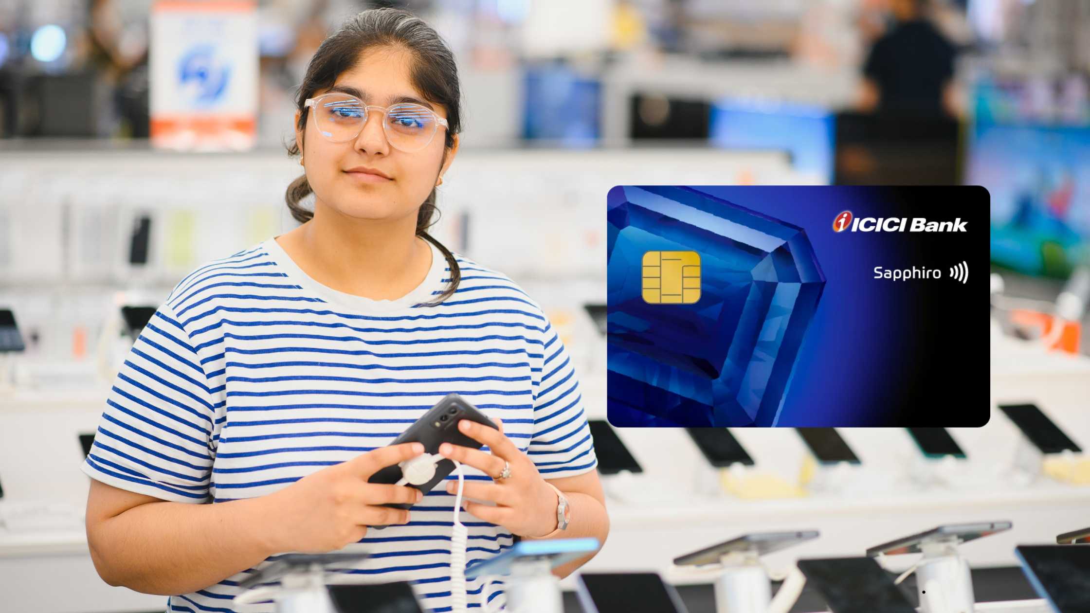 Young woman holding a smartphone in an electronics store, with the blue ICICI Bank Sapphiro Credit Card floating beside her.