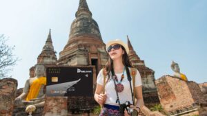 Female tourist with a camera and sunhat at an ancient Buddhist temple site with statues, overlaid with the RBL Bank World Safari Credit Card.