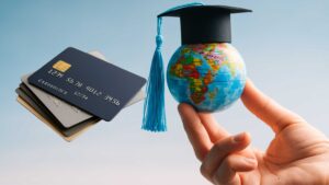 Stack of credit cards next to a small globe wearing a graduation cap, symbolizing students studying abroad and managing international expenses.
