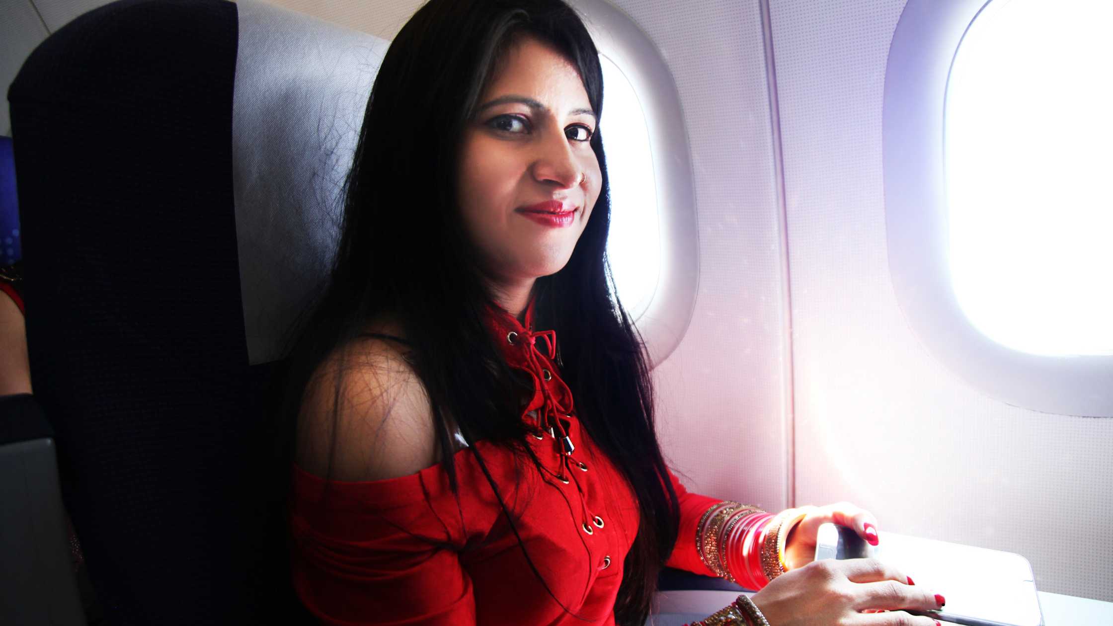 Woman sitting by airplane window with a relaxed smile, traveling on an international flight