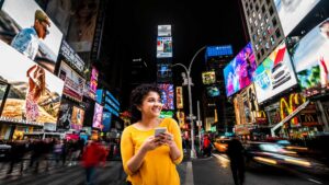 Indian traveler in Times Square using her phone — representing how to use Indian credit card in USA for shopping and payments during international travel.