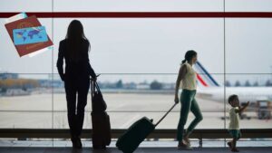 Silhouette of travelers, including a family and a business woman, looking out at an airplane on the tarmac, with a graphic of passports and a credit card overlaid. best credit card with zero forex markup